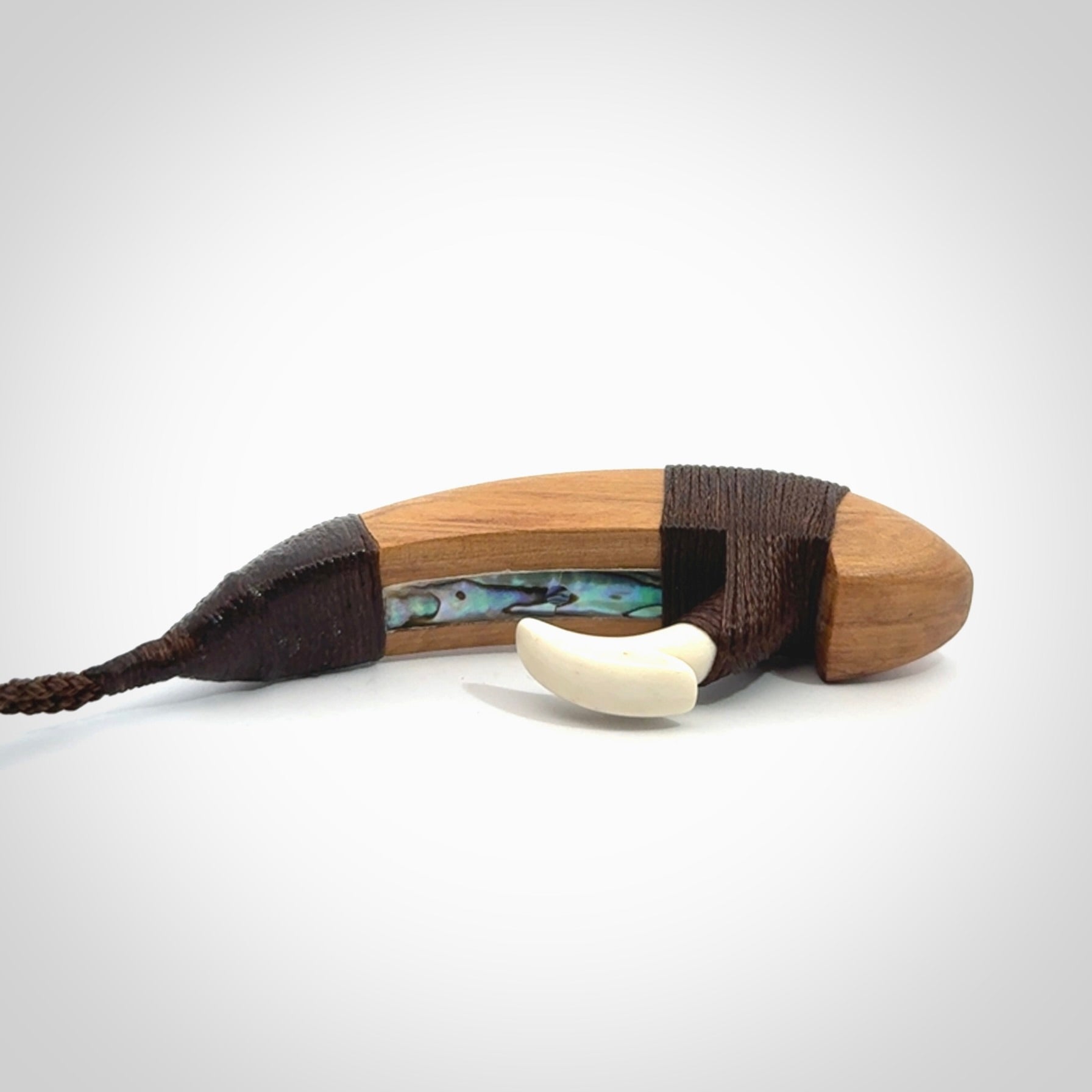 This picture shows a large matau, hook called a pā kahawai. It is carved from bone,  wood, and paua shell. One only, free shipping worldwide. Provided with an adjustable brown cord. Stunning work of Art to Wear by Andrew Doughty.