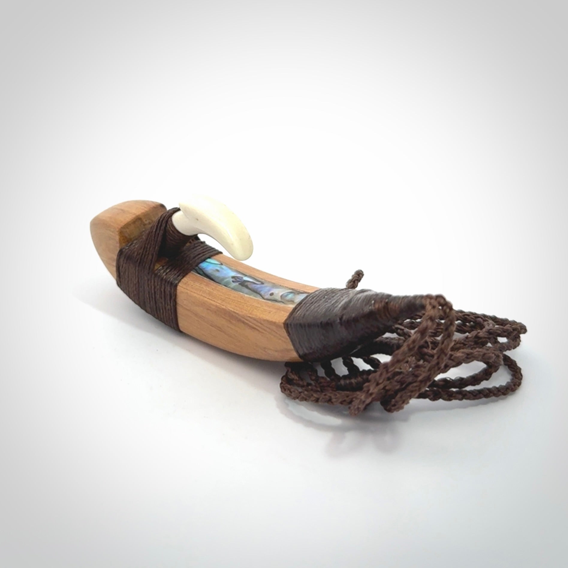 This picture shows a large matau, hook called a pā kahawai. It is carved from bone,  wood, and paua shell. One only, free shipping worldwide. Provided with an adjustable brown cord. Stunning work of Art to Wear by Andrew Doughty.