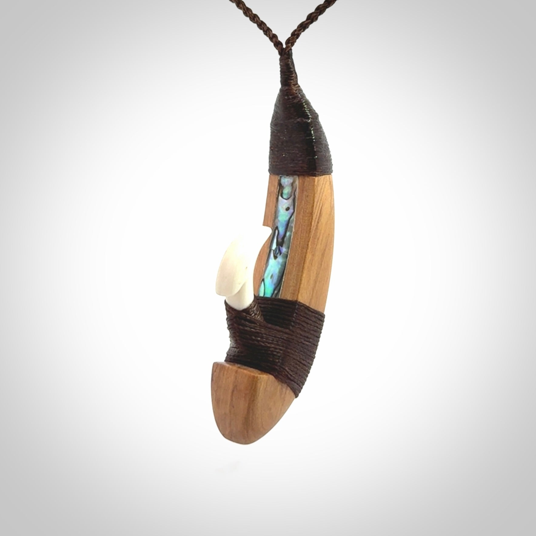 This picture shows a large matau, hook called a pā kahawai. It is carved from bone,  wood, and paua shell. One only, free shipping worldwide. Provided with an adjustable brown cord. Stunning work of Art to Wear by Andrew Doughty.