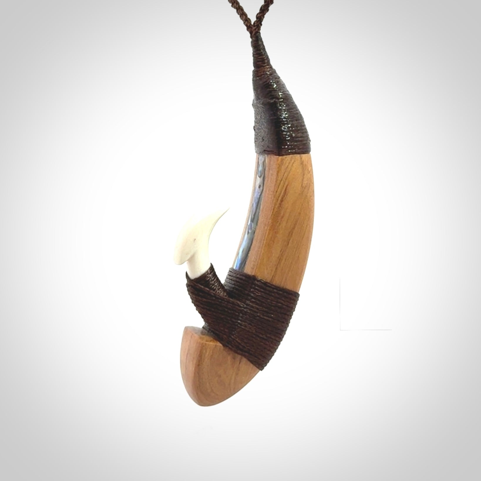 This picture shows a large matau, hook called a pā kahawai. It is carved from bone,  wood, and paua shell. One only, free shipping worldwide. Provided with an adjustable brown cord. Stunning work of Art to Wear by Andrew Doughty.