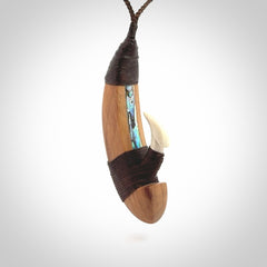 This picture shows a large matau, hook called a pā kahawai. It is carved from bone,  wood, and paua shell. One only, free shipping worldwide. Provided with an adjustable brown cord. Stunning work of Art to Wear by Andrew Doughty.