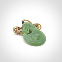 Hand carved New Zealand Inanga jade manaia with koru pendant. Carved from beautiful New Zealand Jade for NZ Pacific by Ross Crump. Unique jade jewellery for sale online. Provided with an adjustable tan cord.