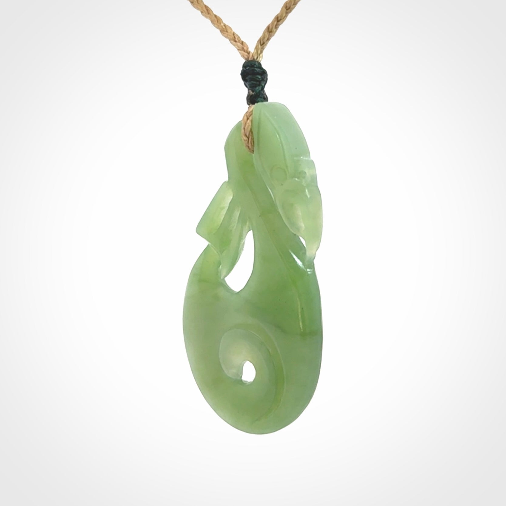 Hand carved New Zealand Inanga jade manaia with koru pendant. Carved from beautiful New Zealand Jade for NZ Pacific by Ross Crump. Unique jade jewellery for sale online. Provided with an adjustable tan cord.