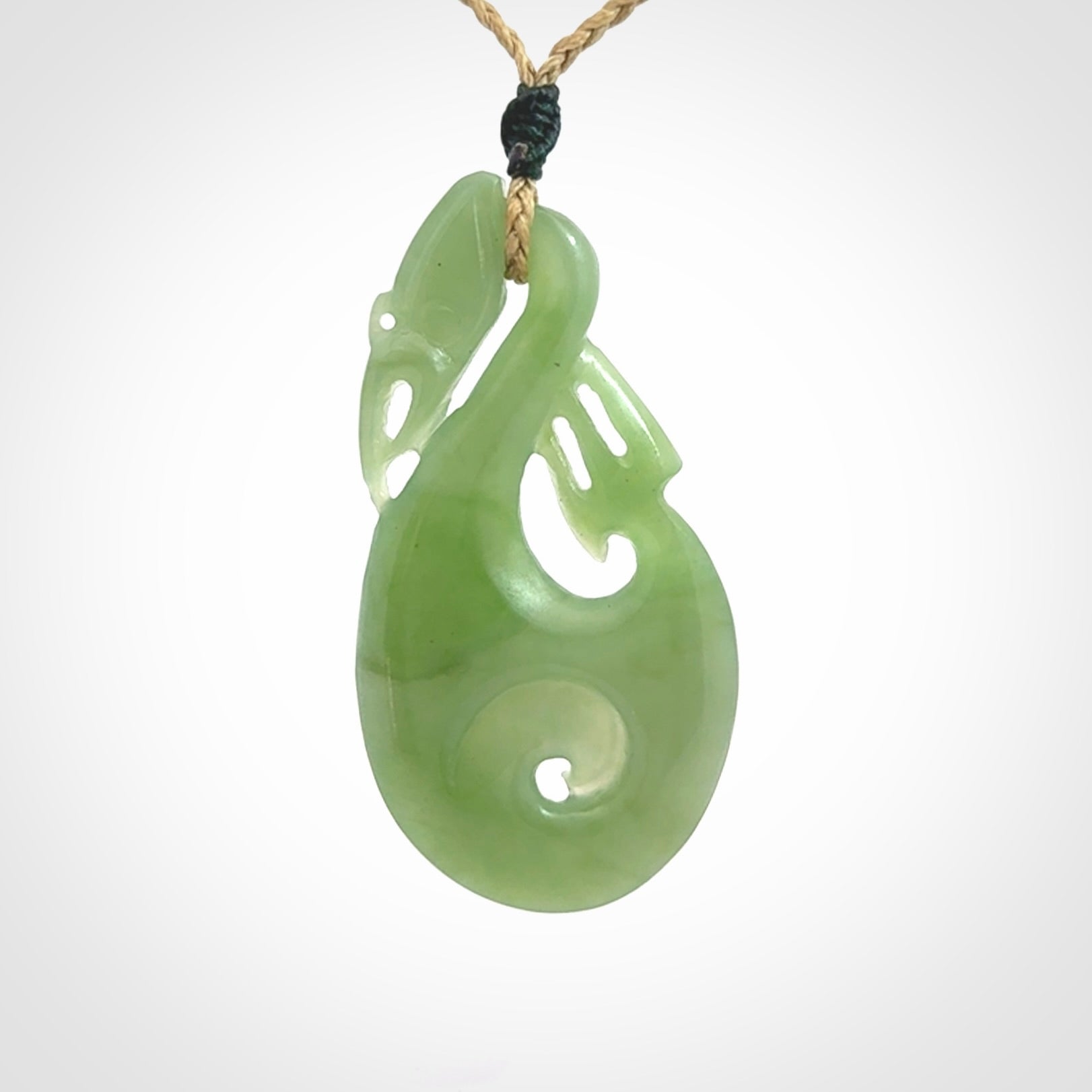 Hand carved New Zealand Inanga jade manaia with koru pendant. Carved from beautiful New Zealand Jade for NZ Pacific by Ross Crump. Unique jade jewellery for sale online. Provided with an adjustable tan cord.