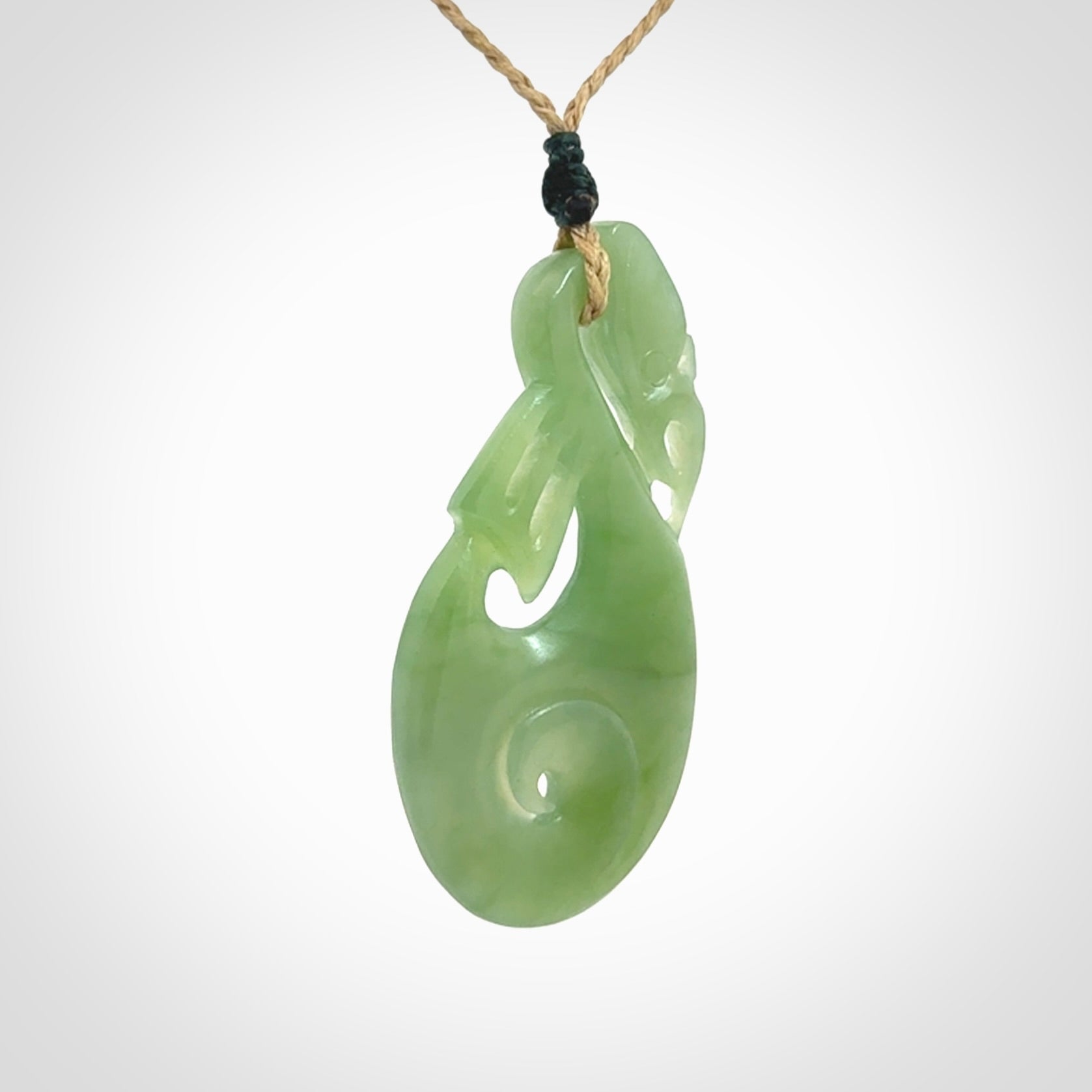 Hand carved New Zealand Inanga jade manaia with koru pendant. Carved from beautiful New Zealand Jade for NZ Pacific by Ross Crump. Unique jade jewellery for sale online. Provided with an adjustable tan cord.