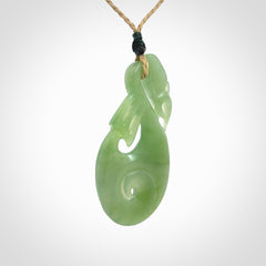 Hand carved New Zealand Inanga jade manaia with koru pendant. Carved from beautiful New Zealand Jade for NZ Pacific by Ross Crump. Unique jade jewellery for sale online. Provided with an adjustable tan cord.