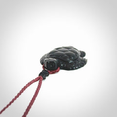 This picture shows a hand carved black jade turtle pendant. It is polished to a soft shine and has quite a lot of detail carved into the jade. The cord is a hand plaited burgundy, waxed polyester. Carved by NZ Pacific.