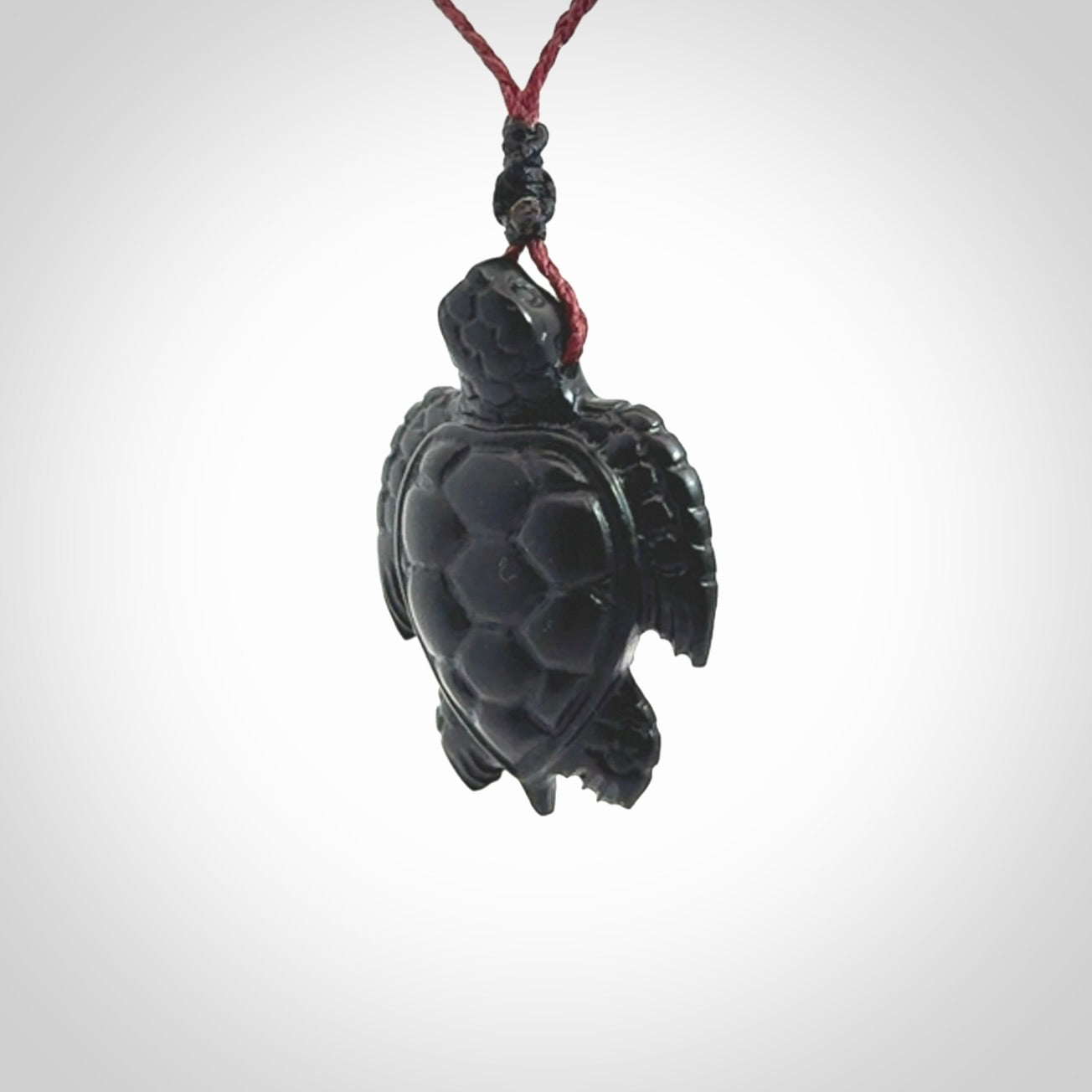 This picture shows a hand carved black jade turtle pendant. It is polished to a soft shine and has quite a lot of detail carved into the jade. The cord is a hand plaited burgundy, waxed polyester. Carved by NZ Pacific.