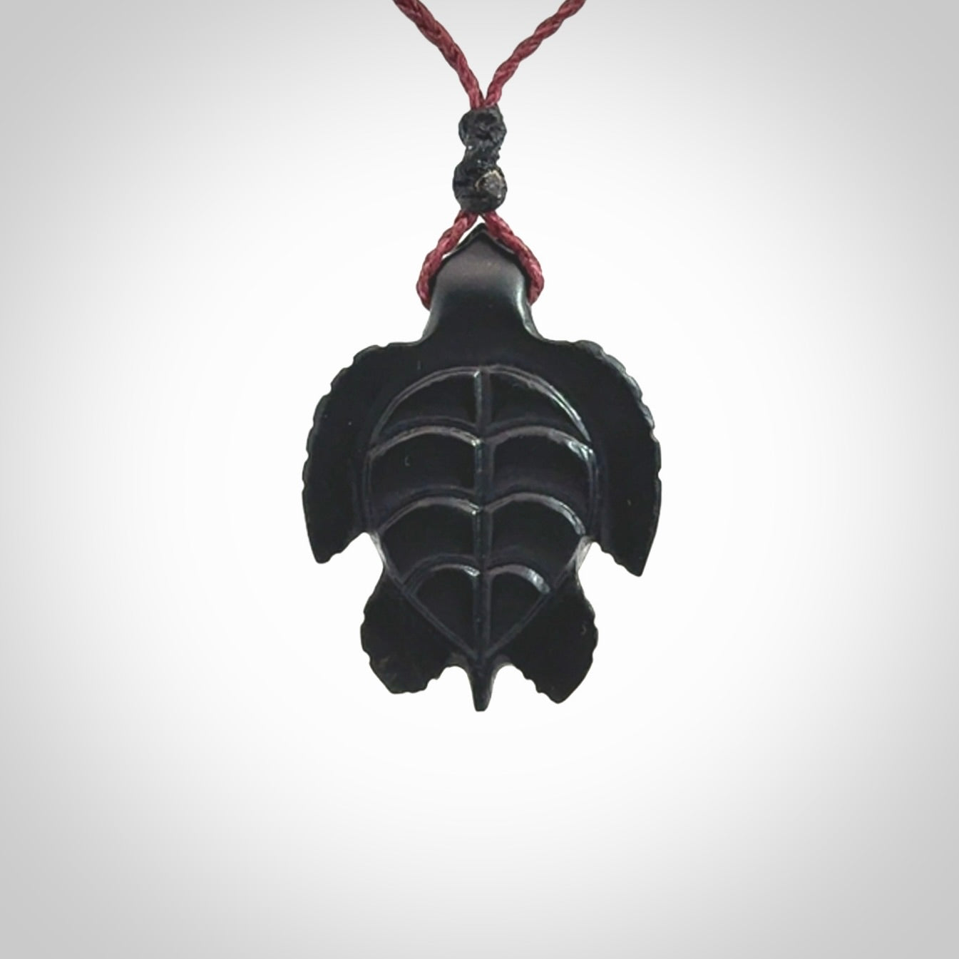 This picture shows a hand carved black jade turtle pendant. It is polished to a soft shine and has quite a lot of detail carved into the jade. The cord is a hand plaited burgundy, waxed polyester. Carved by NZ Pacific.