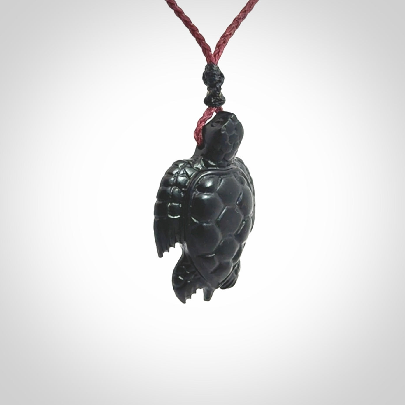 This picture shows a hand carved black jade turtle pendant. It is polished to a soft shine and has quite a lot of detail carved into the jade. The cord is a hand plaited burgundy, waxed polyester. Carved by NZ Pacific.