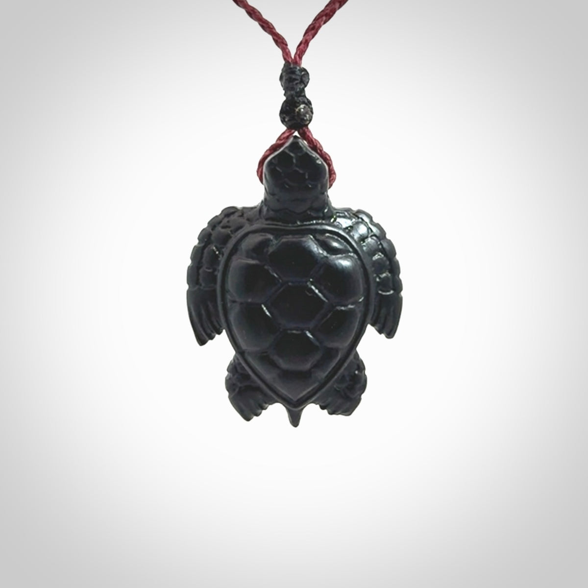 This picture shows a hand carved black jade turtle pendant. It is polished to a soft shine and has quite a lot of detail carved into the jade. The cord is a hand plaited burgundy, waxed polyester. Carved by NZ Pacific.