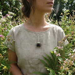 Person wearing a necklace with a pendant in a natural setting