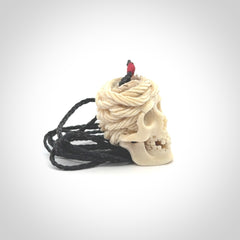 This picture shows a medium sized Deer Antler Bone pirate skull pendant that we have hand carved. The cord is a black colour and has a small red binding just above the pendant.