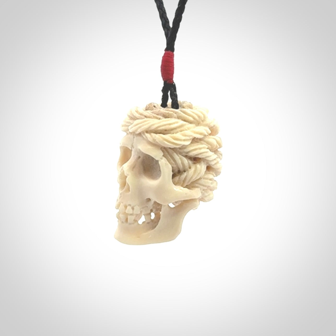 This picture shows a medium sized Deer Antler Bone pirate skull pendant that we have hand carved. The cord is a black colour and has a small red binding just above the pendant.