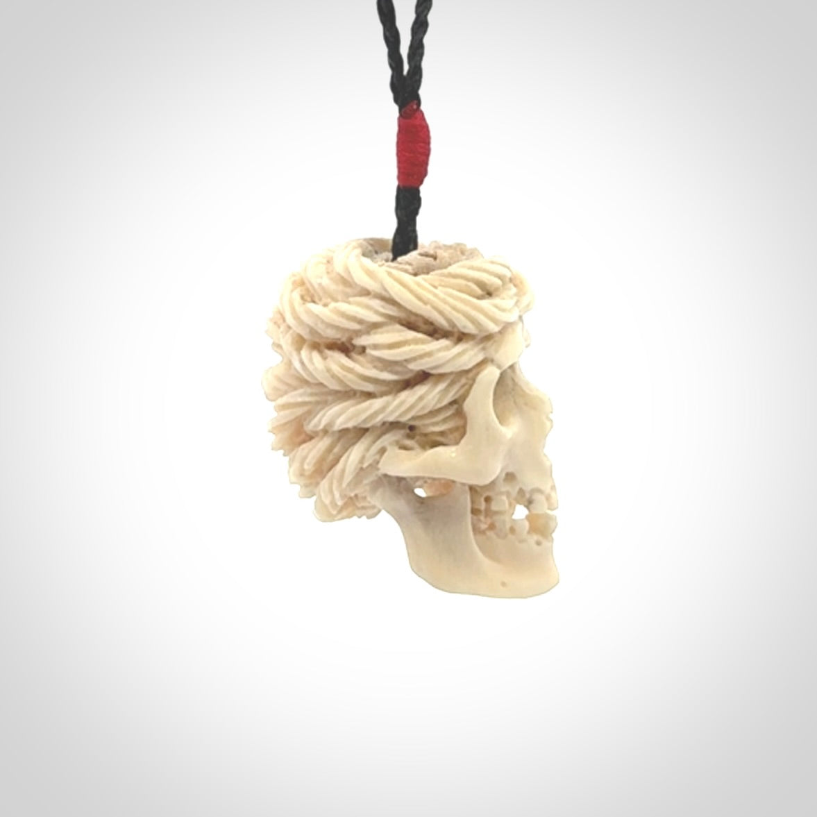 This picture shows a medium sized Deer Antler Bone pirate skull pendant that we have hand carved. The cord is a black colour and has a small red binding just above the pendant.