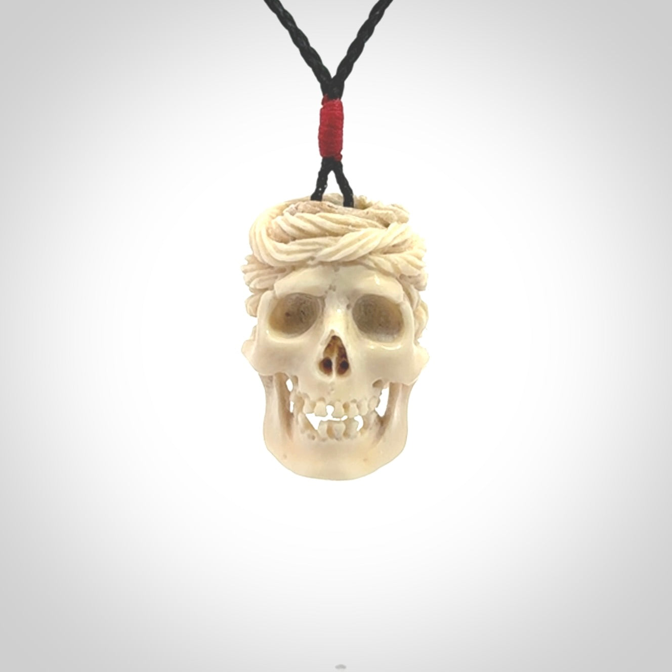 This picture shows a medium sized Deer Antler Bone pirate skull pendant that we have hand carved. The cord is a black colour and has a small red binding just above the pendant.