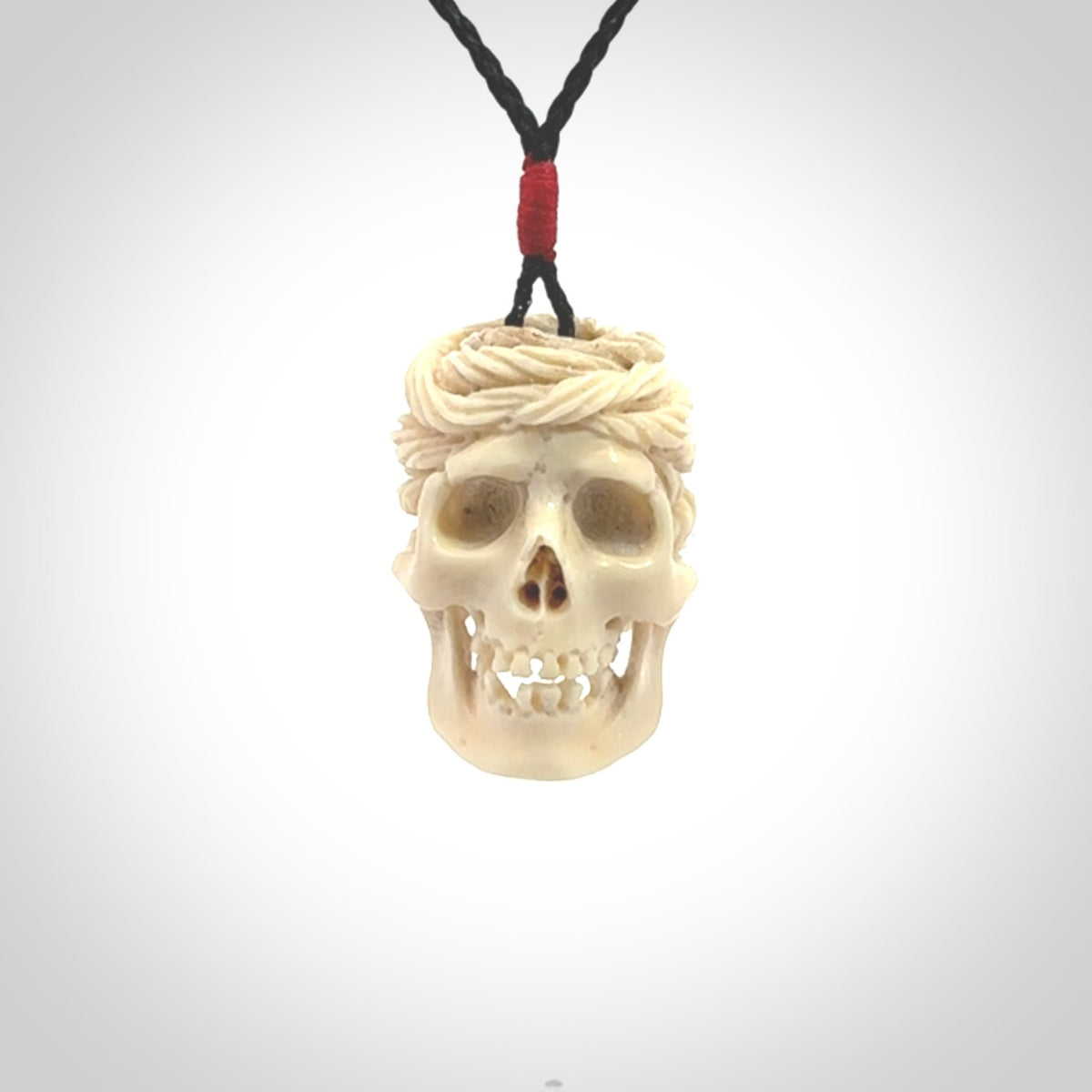 This picture shows a medium sized Deer Antler Bone pirate skull pendant that we have hand carved. The cord is a black colour and has a small red binding just above the pendant.