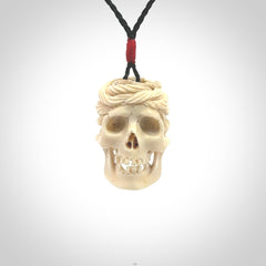 This picture shows a medium sized Deer Antler Bone pirate skull pendant that we have hand carved. The cord is a black colour and has a small red binding just above the pendant.