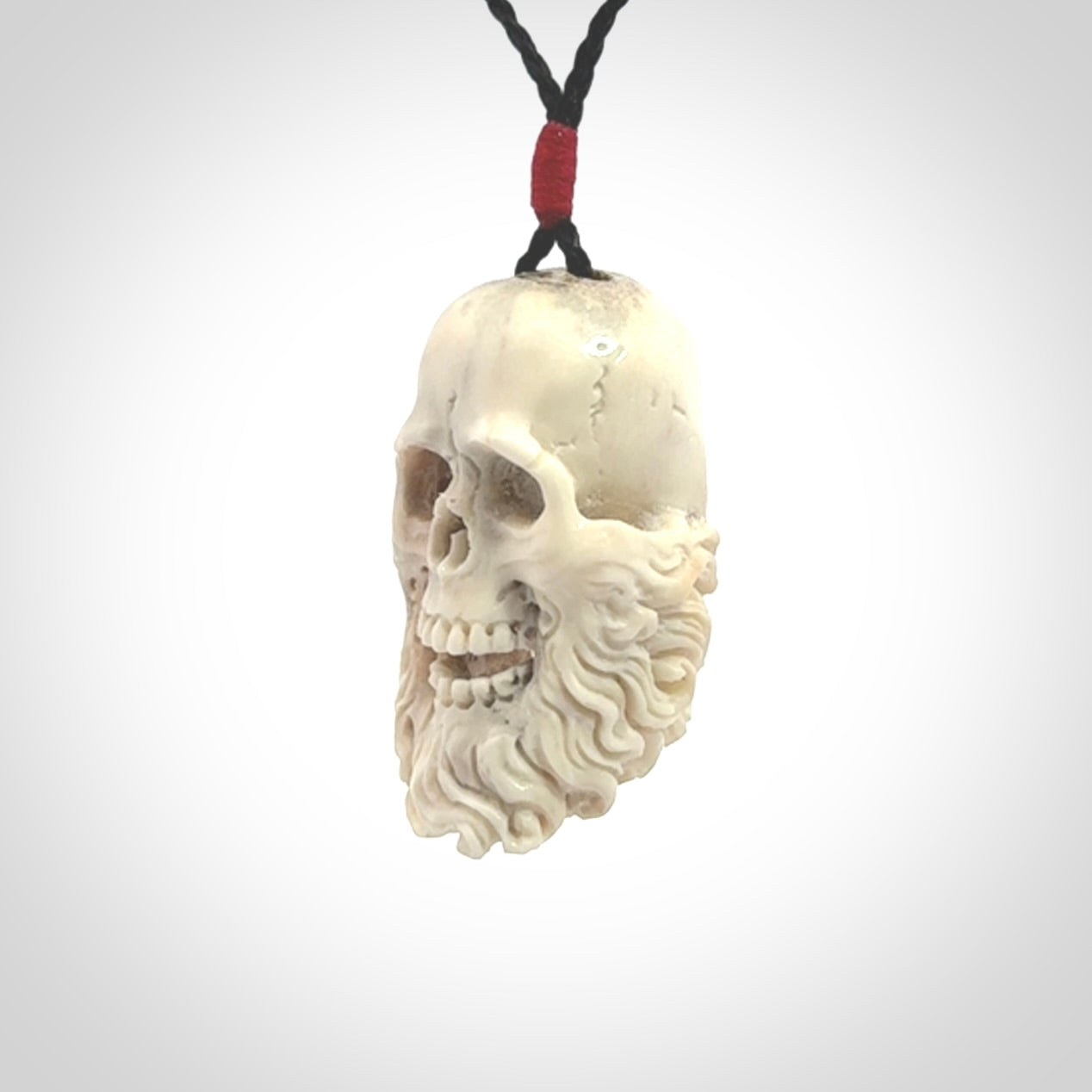 This picture shows a medium sized Deer Antler Bone pirate skull pendant that we have hand carved. The cord is a black colour and has a small red binding just above the pendant.