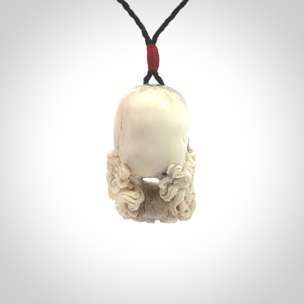 This picture shows a medium sized Deer Antler Bone pirate skull pendant that we have hand carved. The cord is a black colour and has a small red binding just above the pendant.