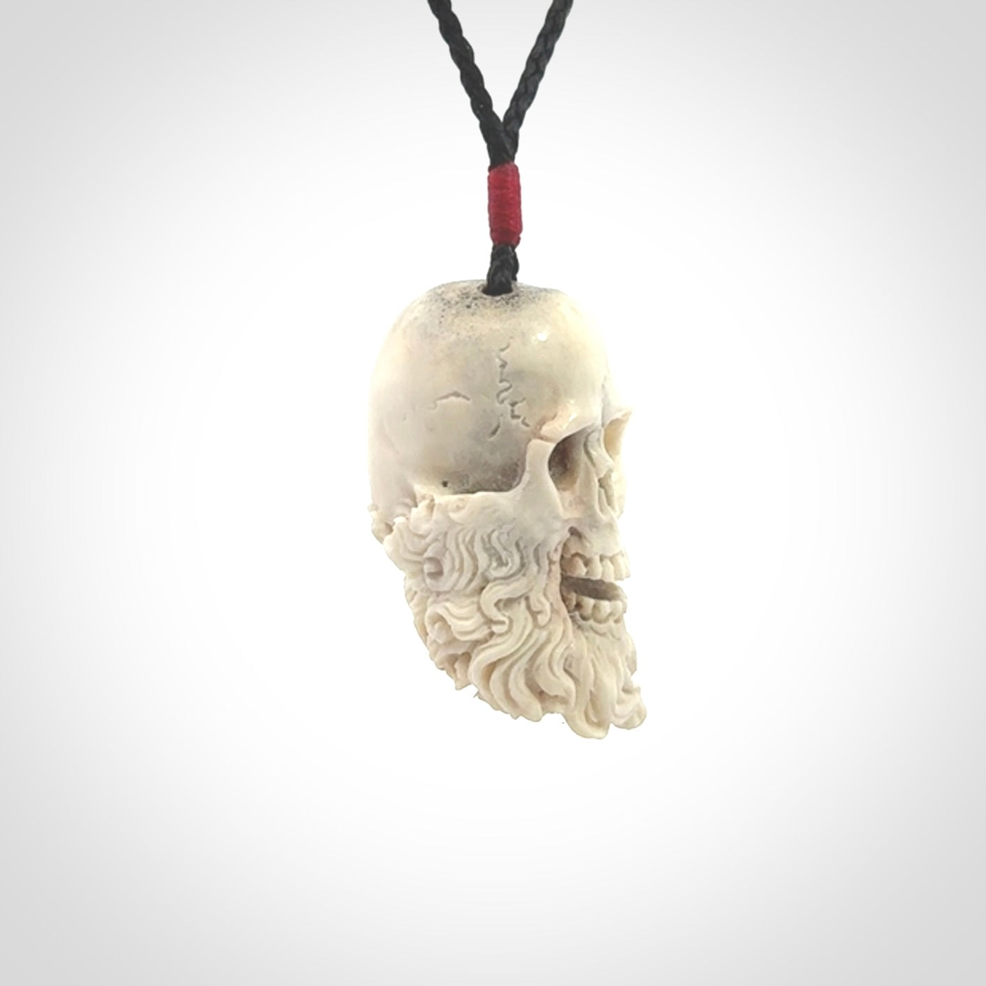 This picture shows a medium sized Deer Antler Bone pirate skull pendant that we have hand carved. The cord is a black colour and has a small red binding just above the pendant.