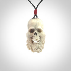 This picture shows a medium sized Deer Antler Bone pirate skull pendant that we have hand carved. The cord is a black colour and has a small red binding just above the pendant.