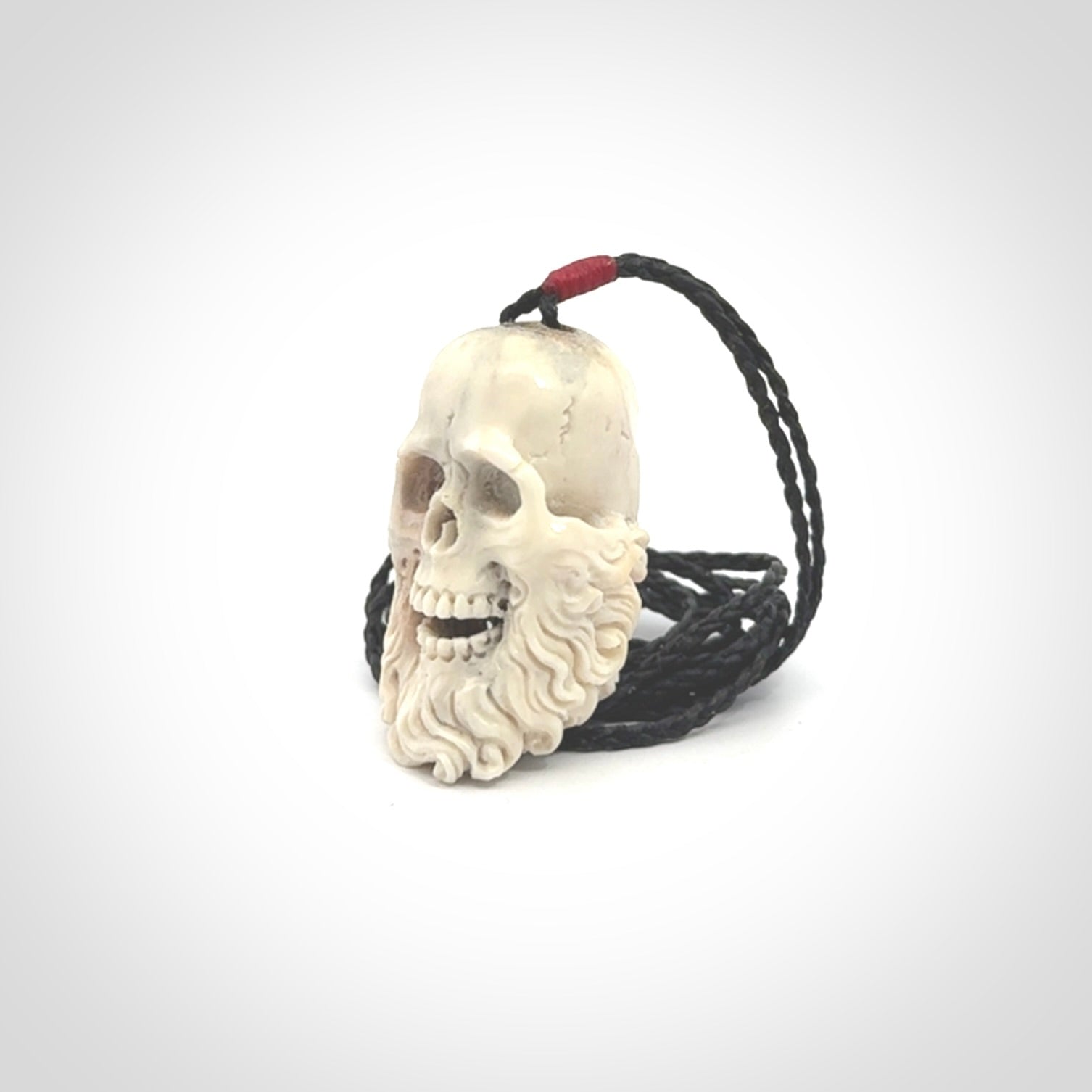 This picture shows a medium sized Deer Antler Bone pirate skull pendant that we have hand carved. The cord is a black colour and has a small red binding just above the pendant.