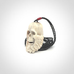 This picture shows a medium sized Deer Antler Bone pirate skull pendant that we have hand carved. The cord is a black colour and has a small red binding just above the pendant.