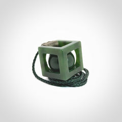 A hand carved medium sized green Jade square box with ball inside necklace. The cord is adjustable in length. A medium sized hand made cube/box with ball necklace in green Jade.