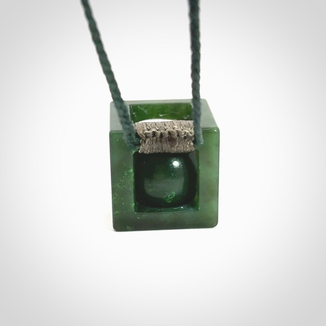 A hand carved medium sized green Jade square box with ball inside necklace. The cord is adjustable in length. A medium sized hand made cube/box with ball necklace in green Jade.