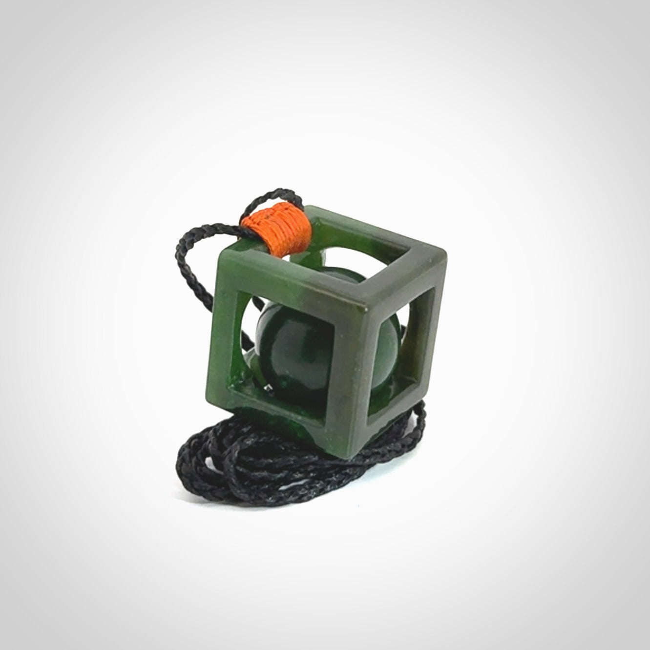 A hand carved medium sized green Jade square box with ball inside necklace. The cord is adjustable in length. A medium sized hand made cube/box with ball necklace in green Jade.