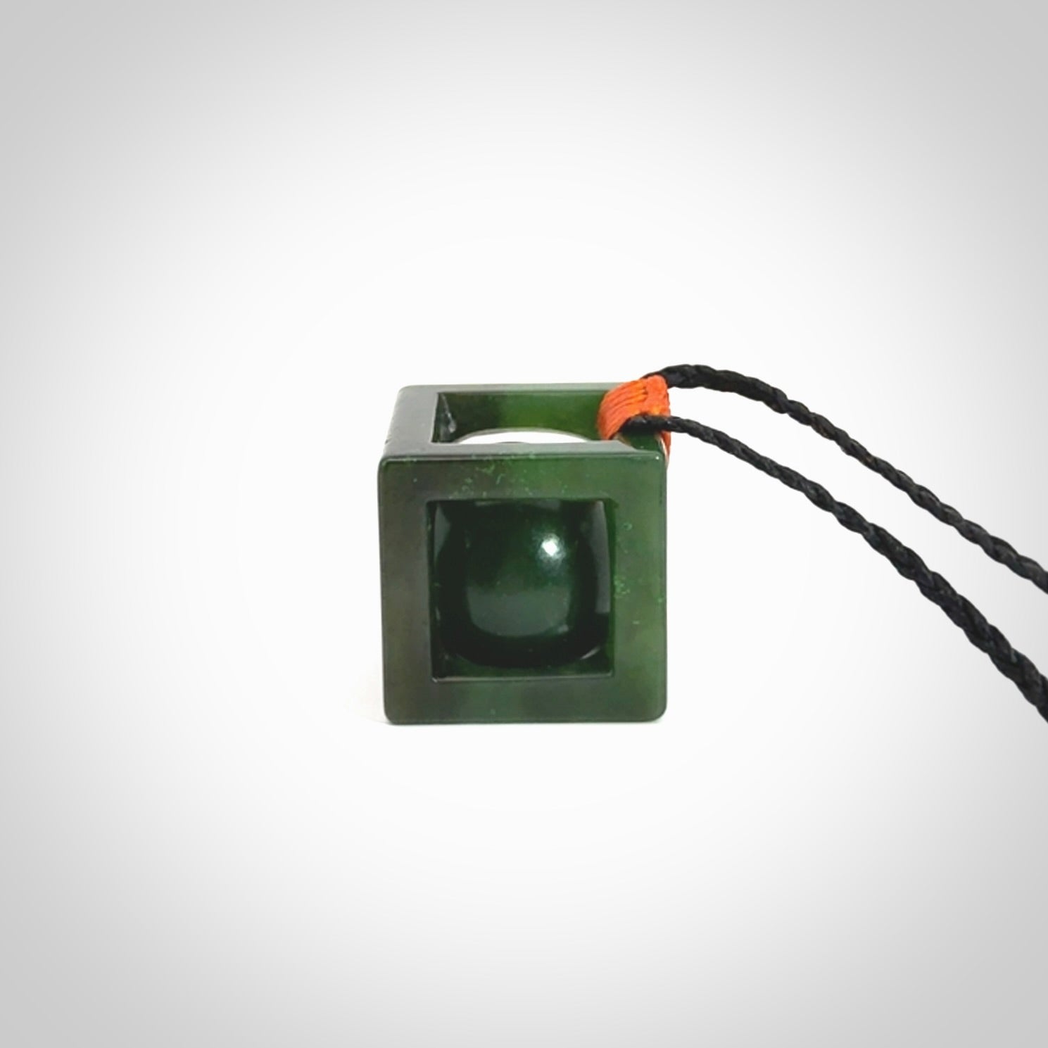A hand carved medium sized green Jade square box with ball inside necklace. The cord is adjustable in length. A medium sized hand made cube/box with ball necklace in green Jade.
