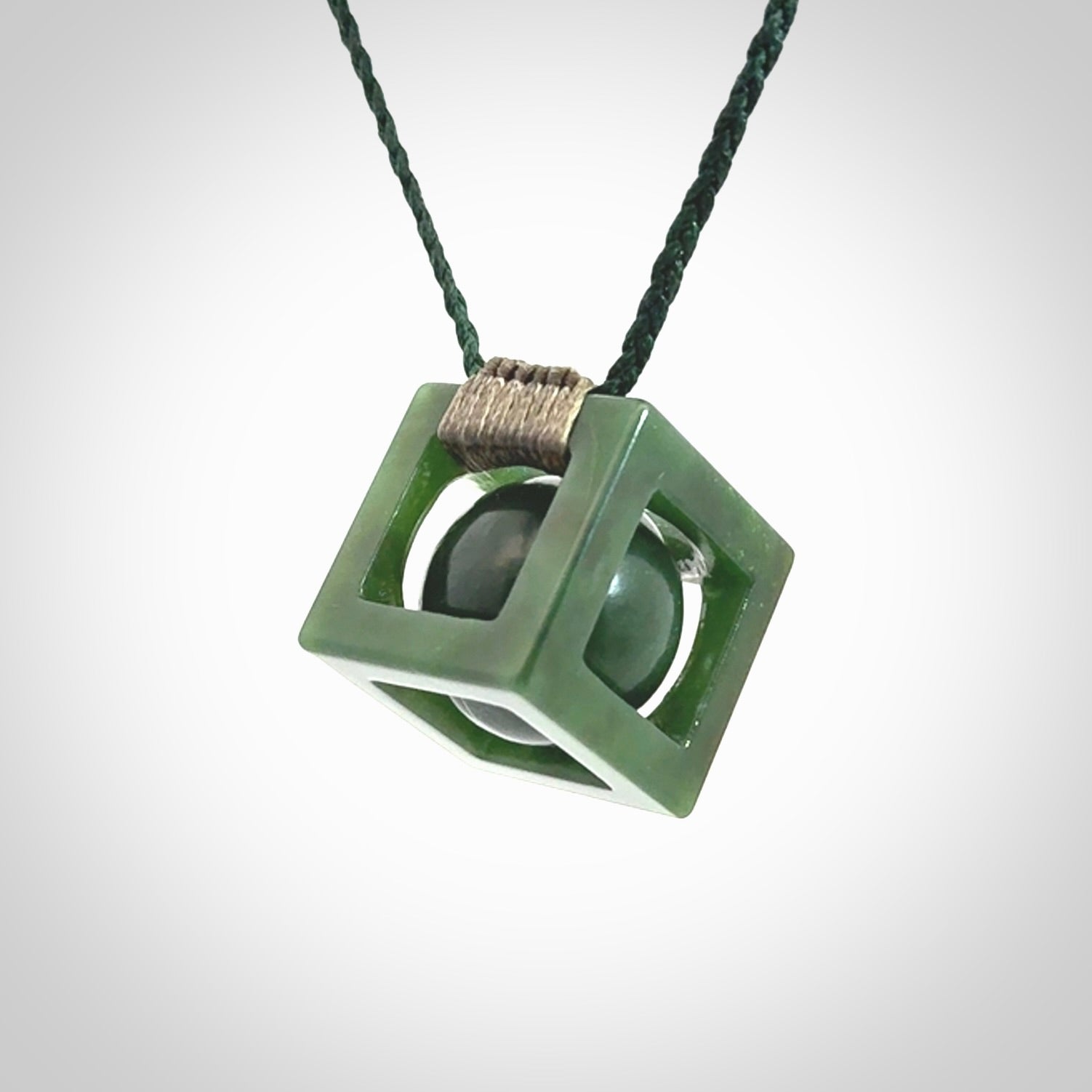 A hand carved medium sized green Jade square box with ball inside necklace. The cord is adjustable in length. A medium sized hand made cube/box with ball necklace in green Jade.