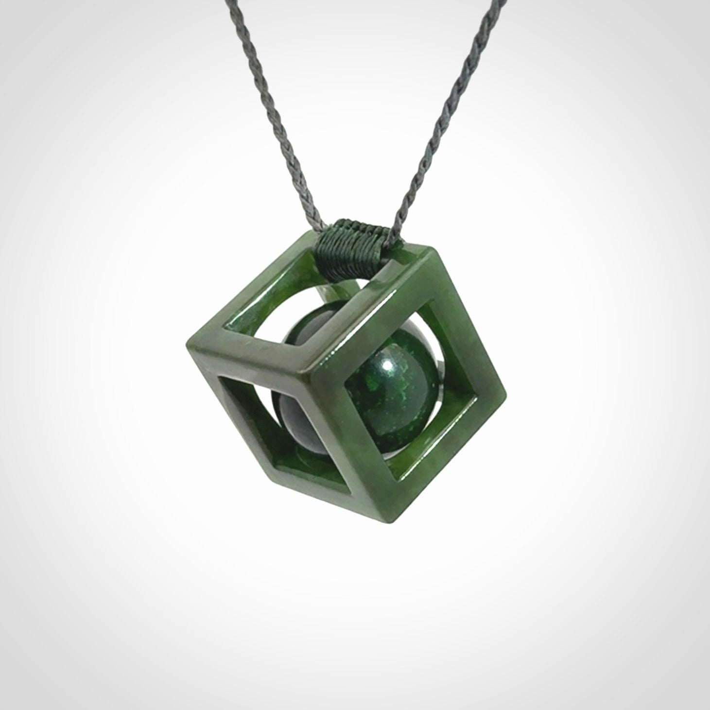 A hand carved medium sized green Jade square box with ball inside necklace. The cord is adjustable in length. A medium sized hand made cube/box with ball necklace in green Jade.