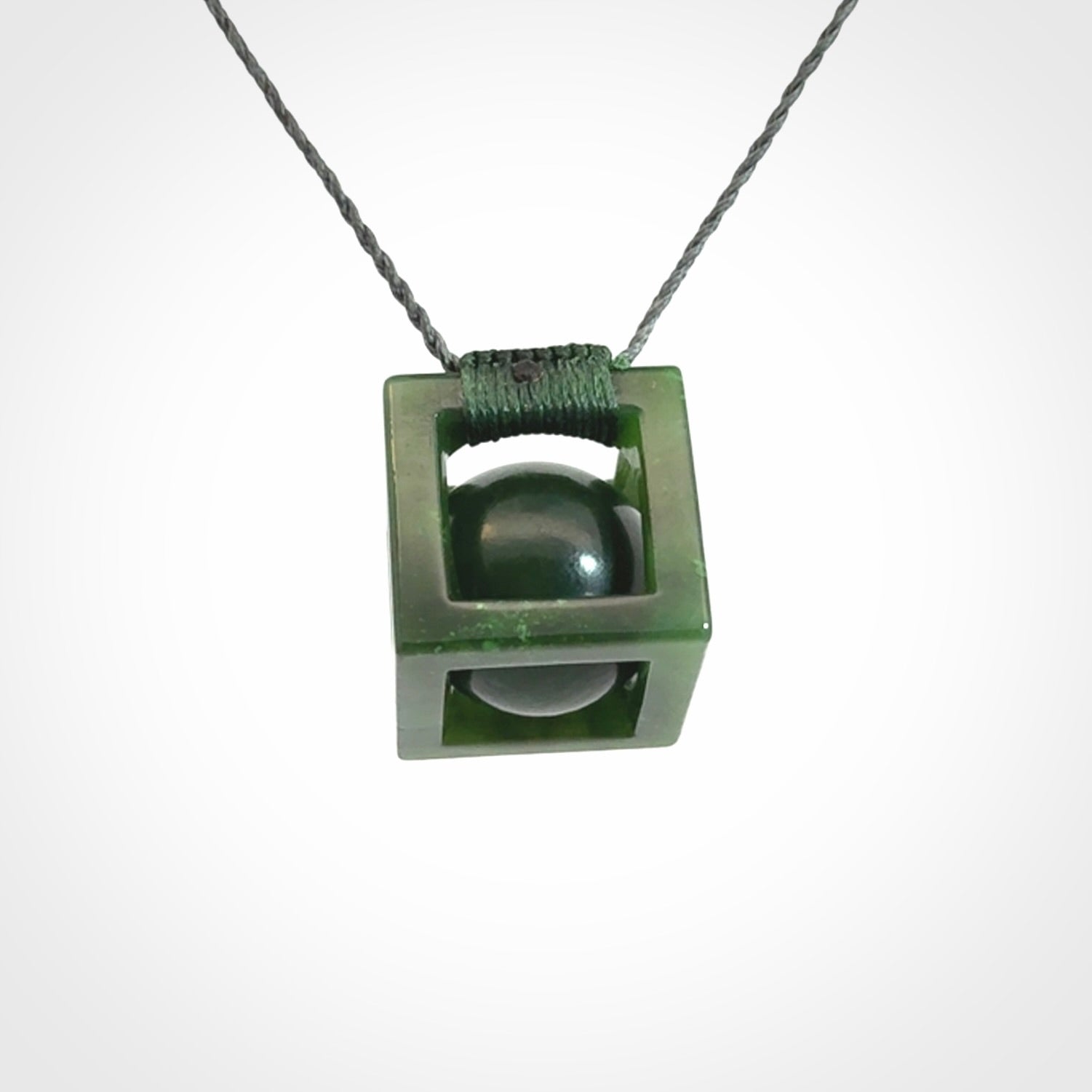 A hand carved medium sized green Jade square box with ball inside necklace. The cord is adjustable in length. A medium sized hand made cube/box with ball necklace in green Jade.