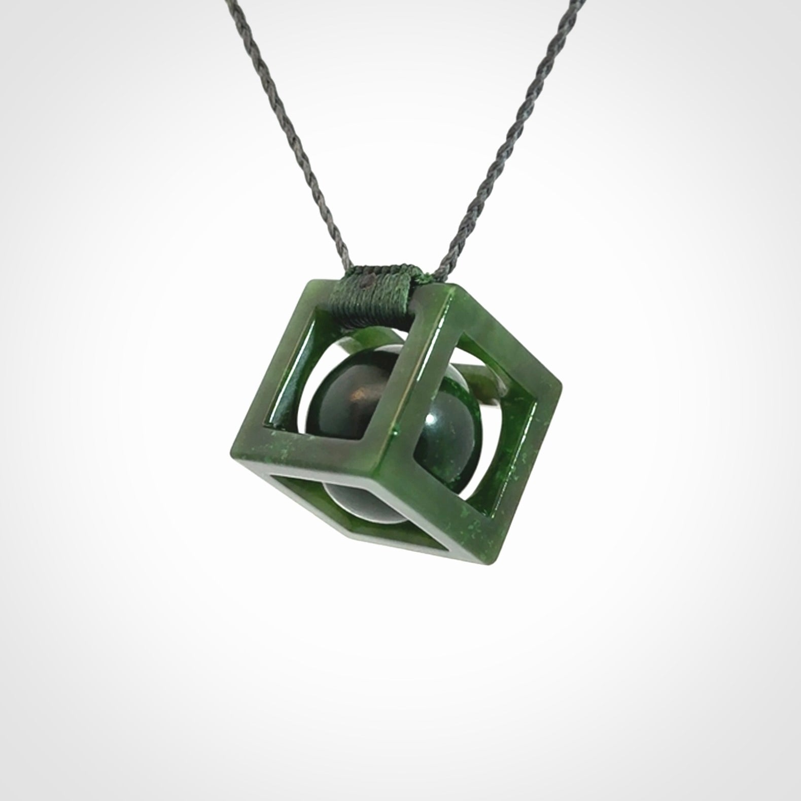 A hand carved medium sized green Jade square box with ball inside necklace. The cord is adjustable in length. A medium sized hand made cube/box with ball necklace in green Jade.