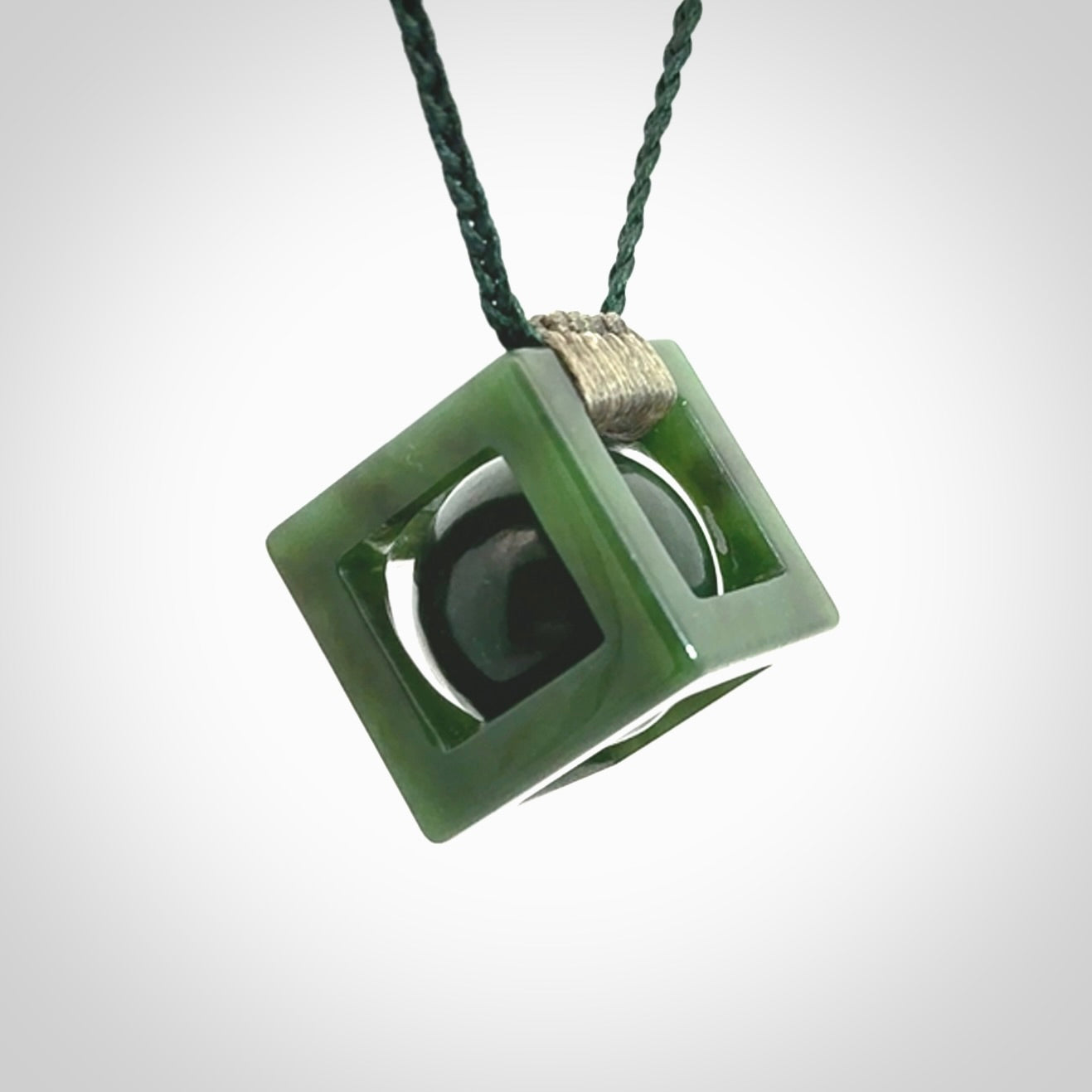 A hand carved medium sized green Jade square box with ball inside necklace. The cord is adjustable in length. A medium sized hand made cube/box with ball necklace in green Jade.
