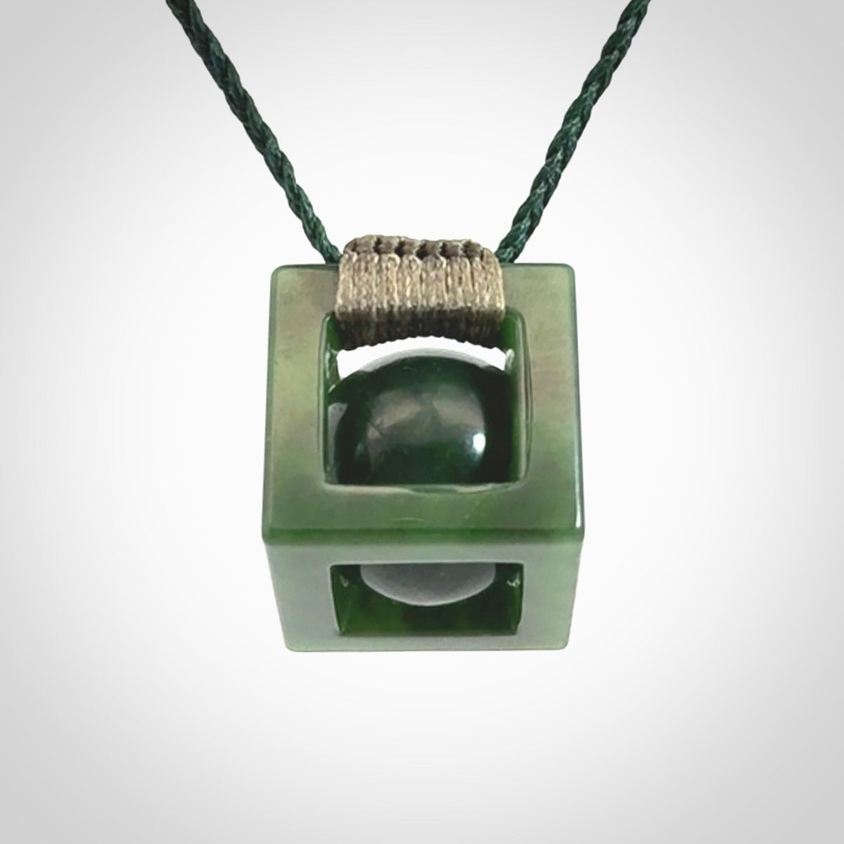 A hand carved medium sized green Jade square box with ball inside necklace. The cord is adjustable in length. A medium sized hand made cube/box with ball necklace in green Jade.