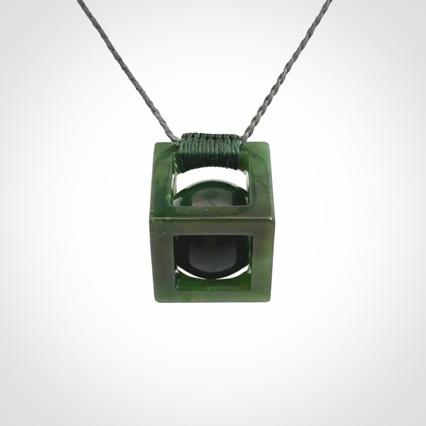 A hand carved medium sized green Jade square box with ball inside necklace. The cord is adjustable in length. A medium sized hand made cube/box with ball necklace in green Jade.