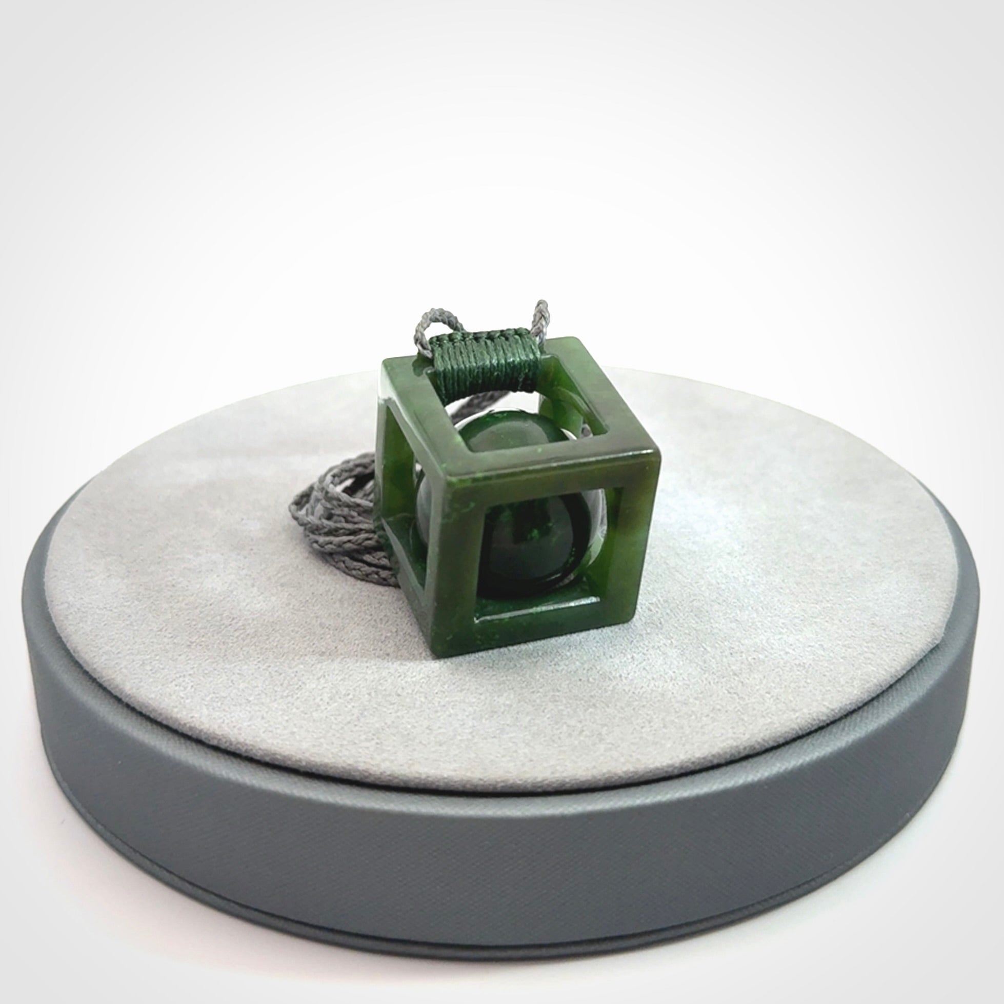 A hand carved medium sized green Jade square box with ball inside necklace. The cord is adjustable in length. A medium sized hand made cube/box with ball necklace in green Jade.
