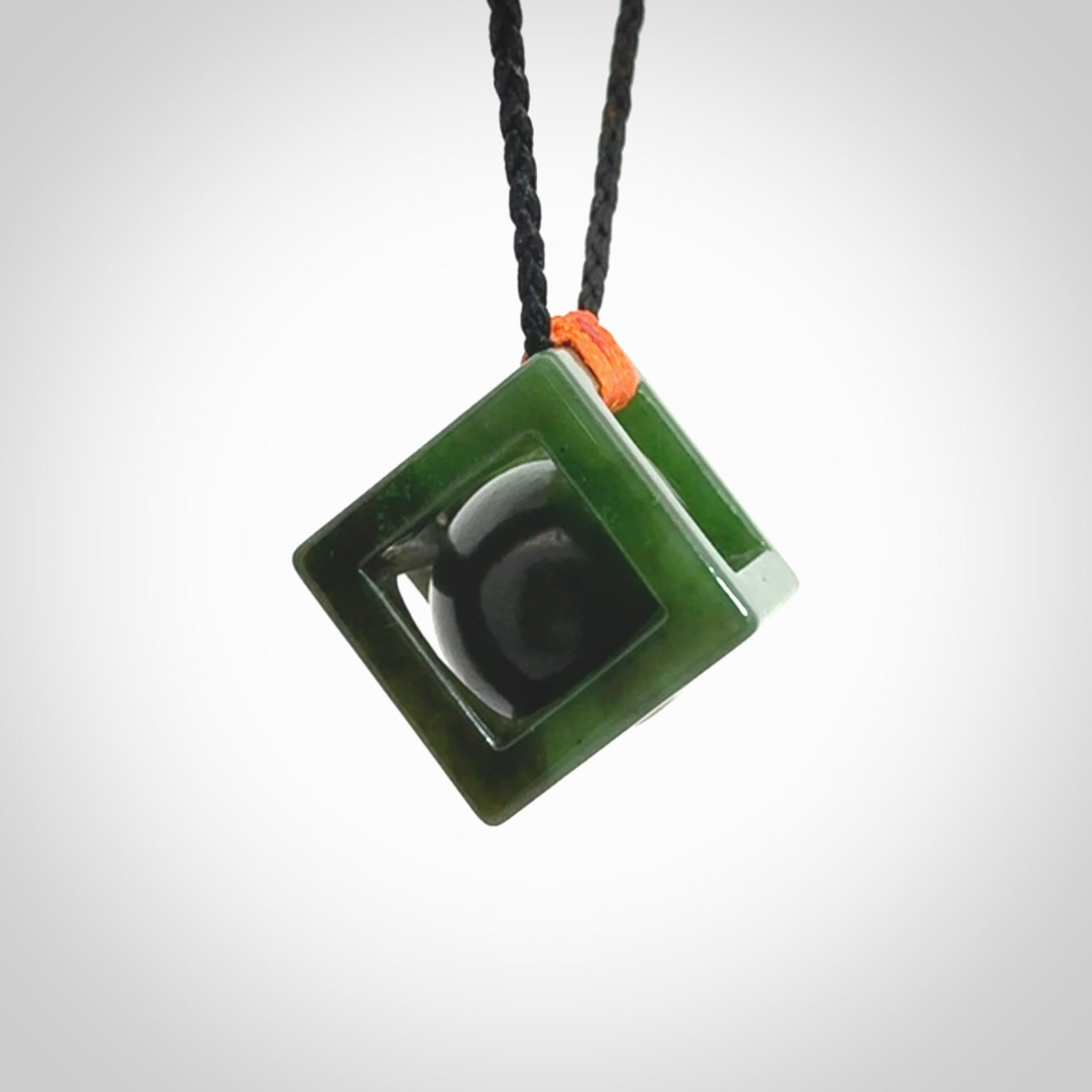 A hand carved medium sized green Jade square box with ball inside necklace. The cord is adjustable in length. A medium sized hand made cube/box with ball necklace in green Jade.