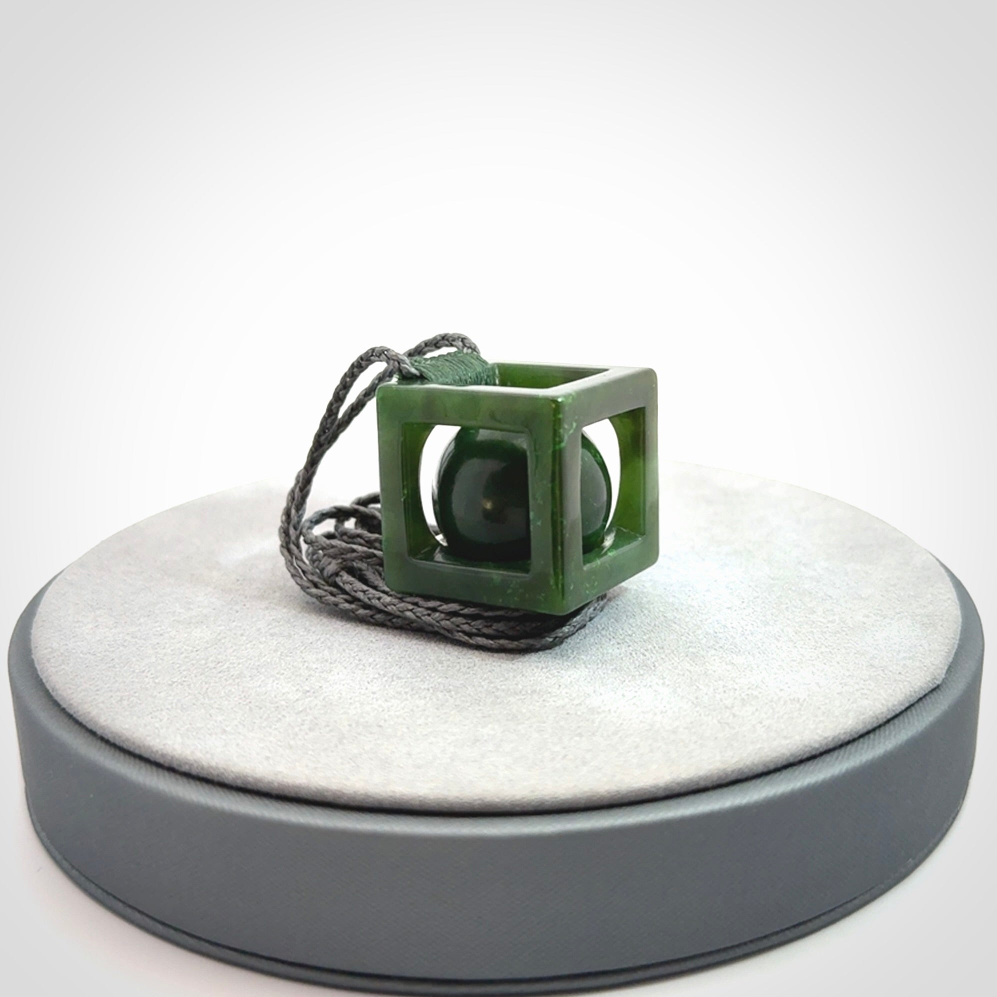 A hand carved medium sized green Jade square box with ball inside necklace. The cord is adjustable in length. A medium sized hand made cube/box with ball necklace in green Jade.