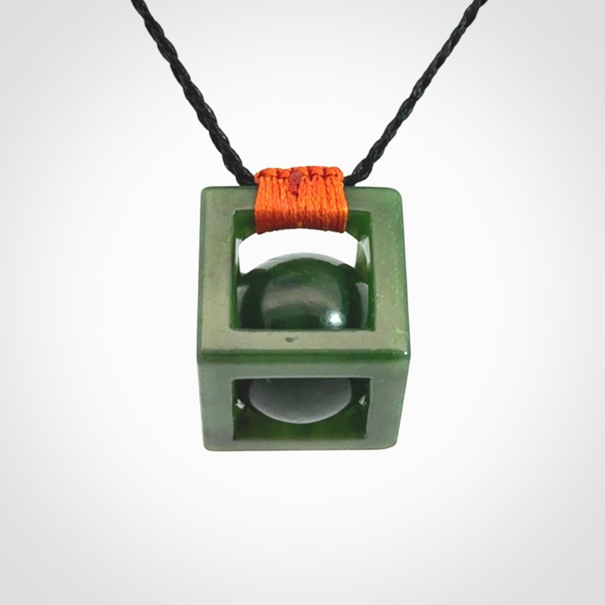 A hand carved medium sized green Jade square box with ball inside necklace. The cord is adjustable in length. A medium sized hand made cube/box with ball necklace in green Jade.