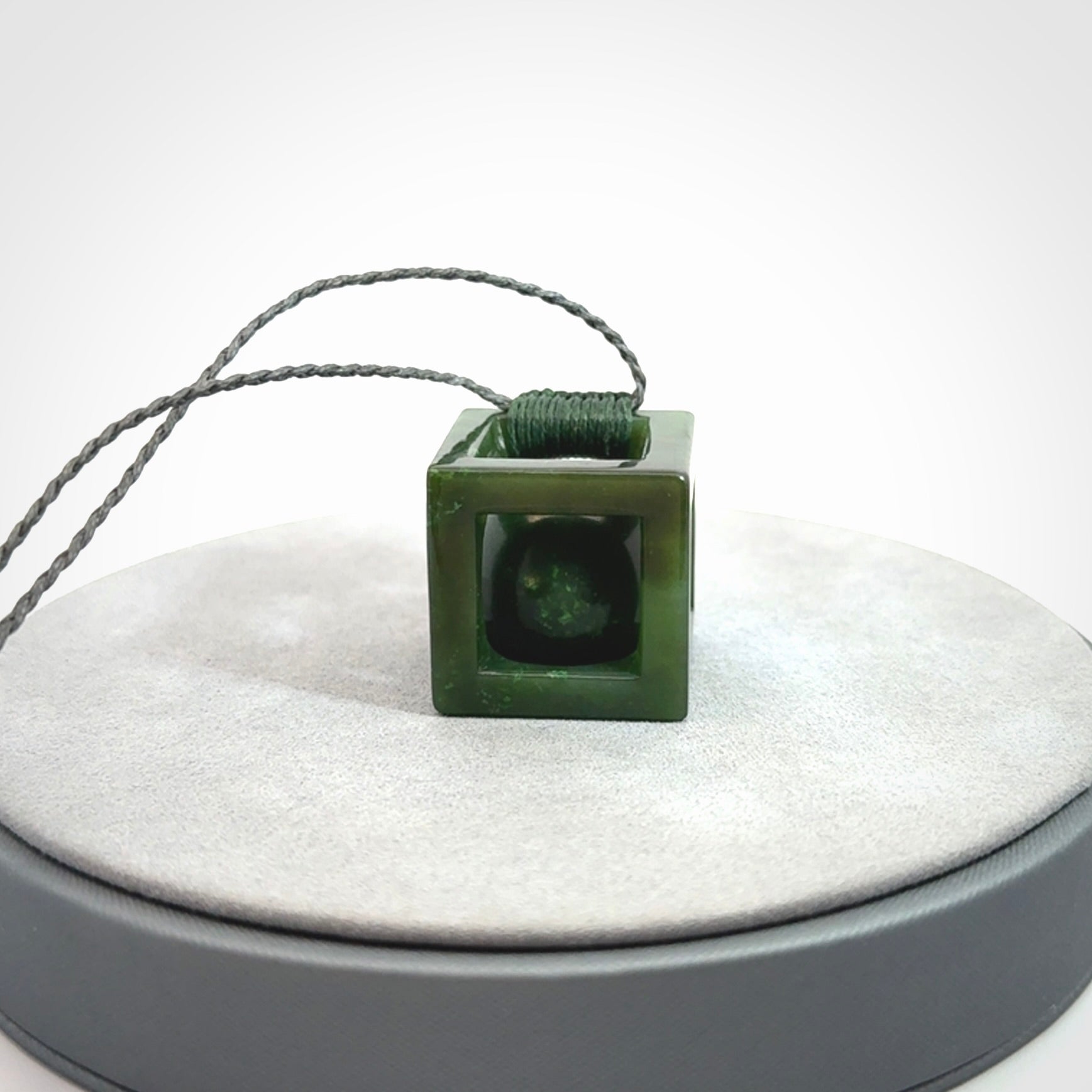 A hand carved medium sized green Jade square box with ball inside necklace. The cord is adjustable in length. A medium sized hand made cube/box with ball necklace in green Jade.