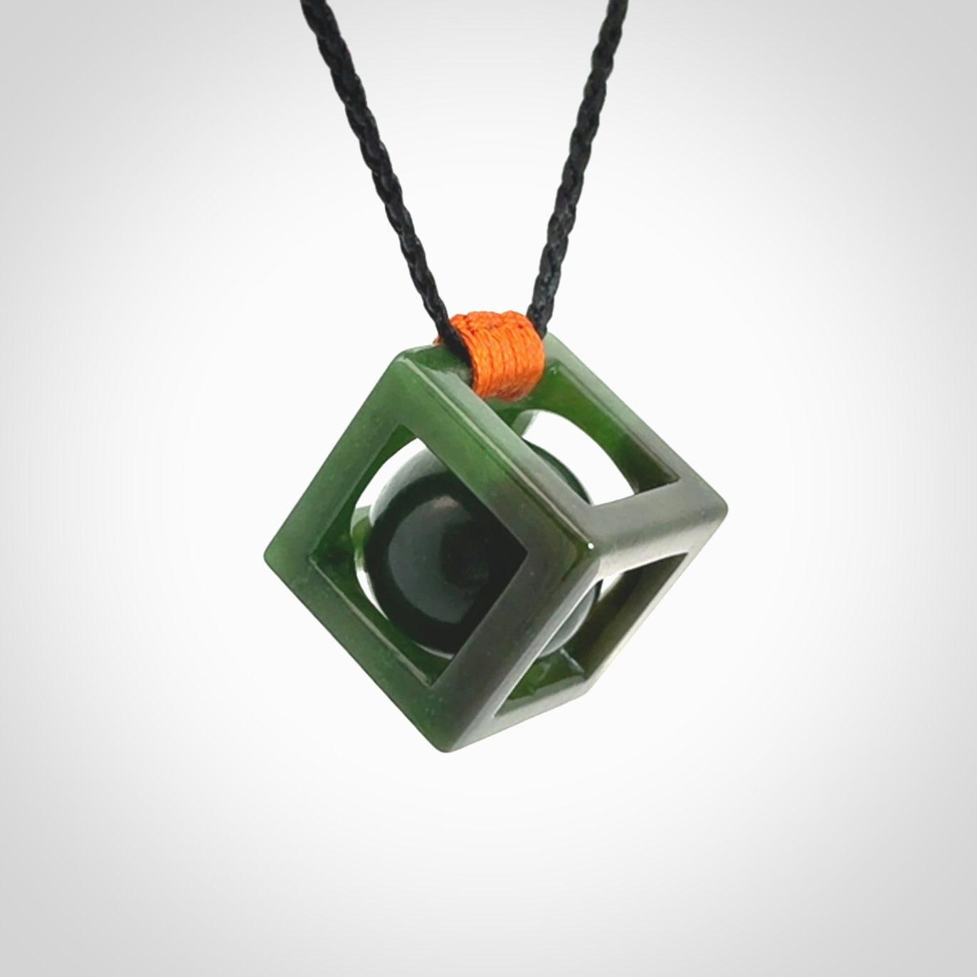 A hand carved medium sized green Jade square box with ball inside necklace. The cord is adjustable in length. A medium sized hand made cube/box with ball necklace in green Jade.