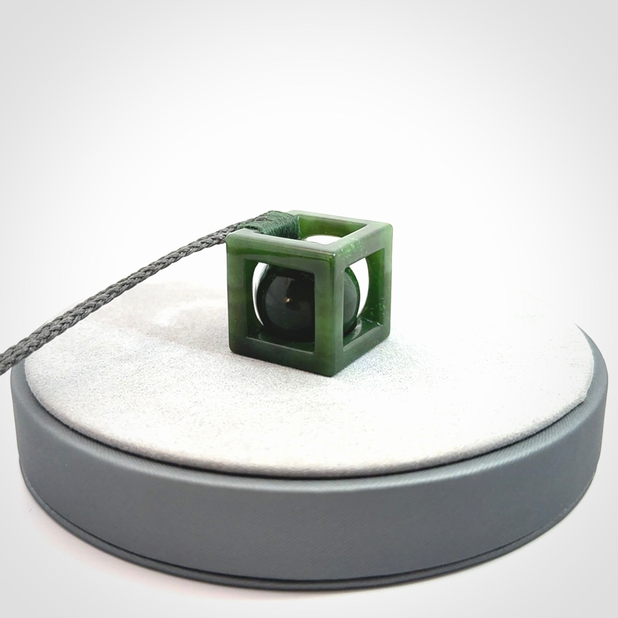 A hand carved medium sized green Jade square box with ball inside necklace. The cord is adjustable in length. A medium sized hand made cube/box with ball necklace in green Jade.