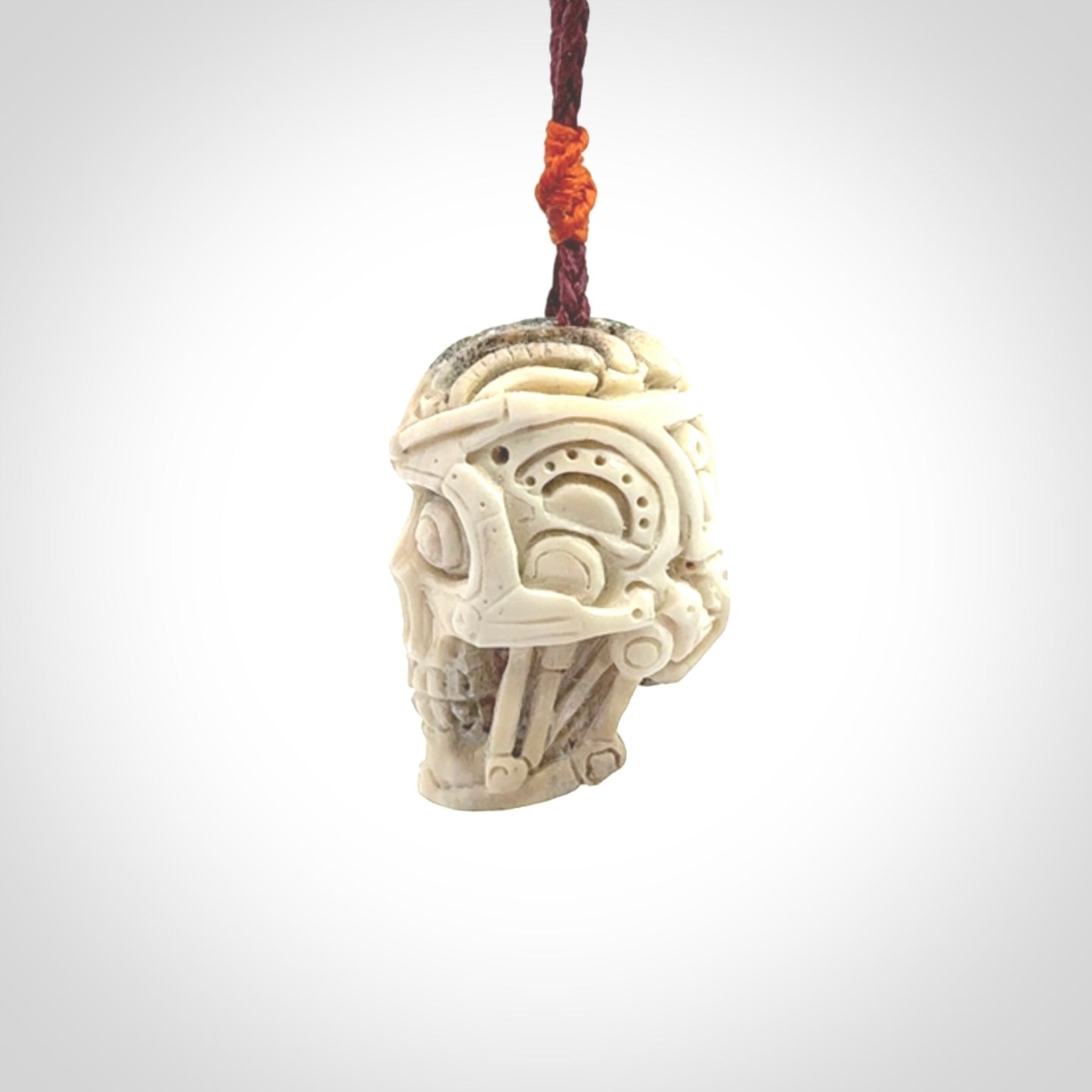 This picture shows a medium sized Deer Antler Bone robot skull pendant that we have hand carved. The cord is a plum colour and has a small orange binding just above the pendant.