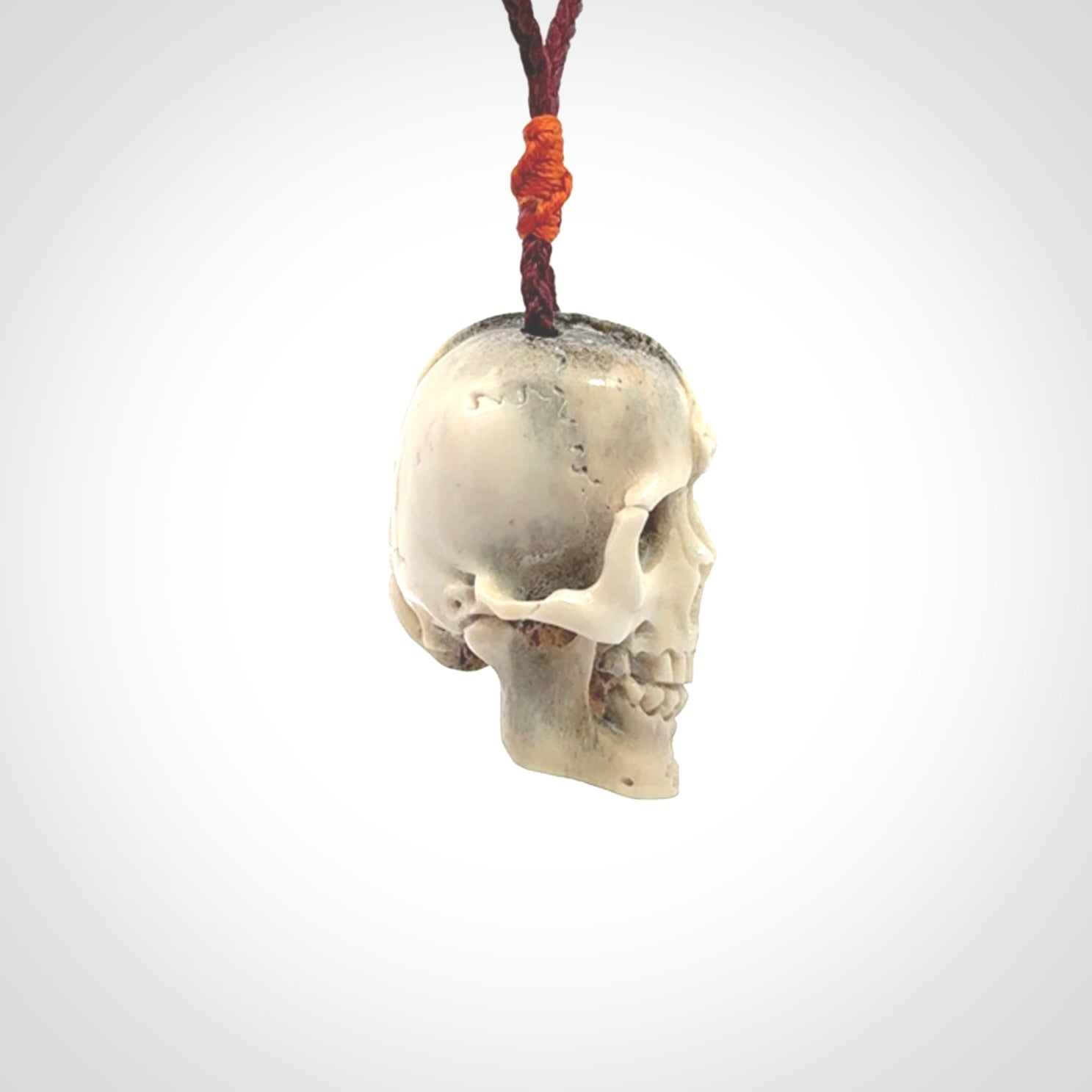 This picture shows a medium sized Deer Antler Bone robot skull pendant that we have hand carved. The cord is a plum colour and has a small orange binding just above the pendant.