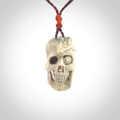 This picture shows a medium sized Deer Antler Bone robot skull pendant that we have hand carved. The cord is a plum colour and has a small orange binding just above the pendant.