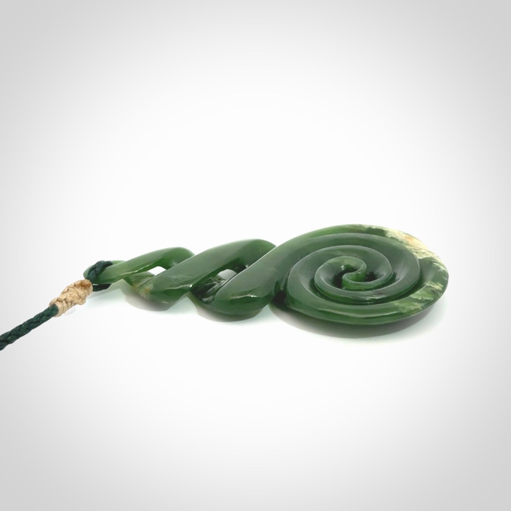 Ross Crump triple twist with koru pendant. Hand carved from rare New Zealand jade this is a beautiful pounamu pendant. The cord is length adjustable. It is a delicate and very beautiful greenstone pendant. For sale online by NZ Pacific.